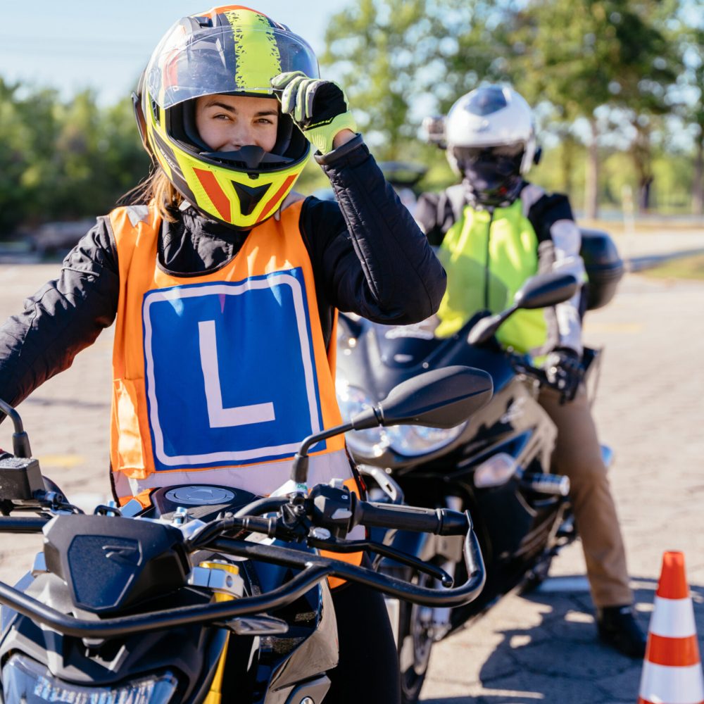 Woman L-driver and instructor motorcycle school doing exercise around cones on the motorbike in skill training motordrome. Concept of motorcycle school of driving