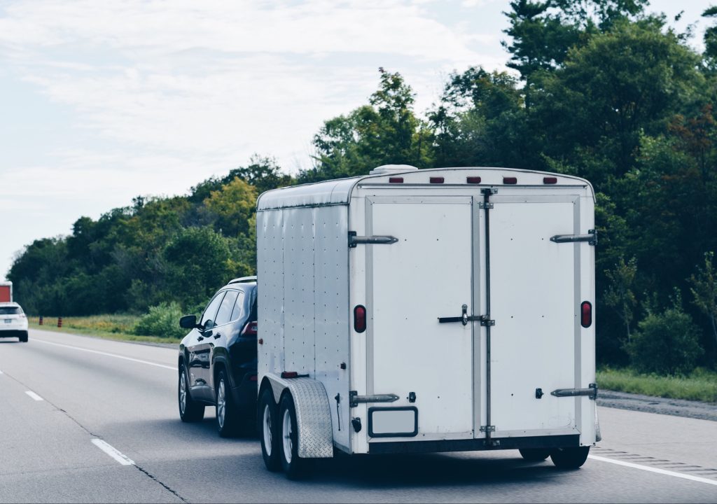 Trailer attached to a car driving on a highway carrying furniture and personal belongings